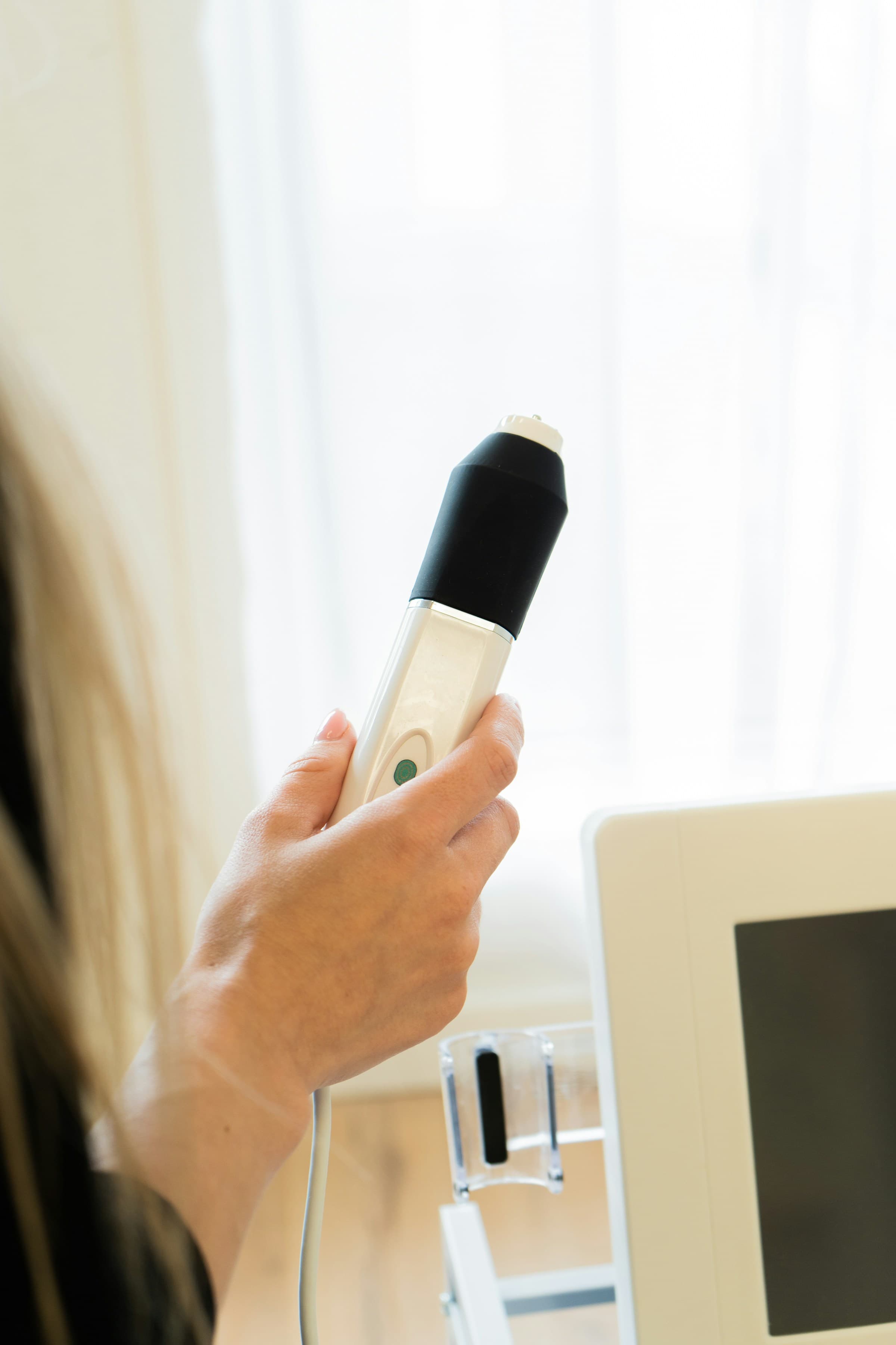 Hand holding a skincare technology device beside a treatment monitor